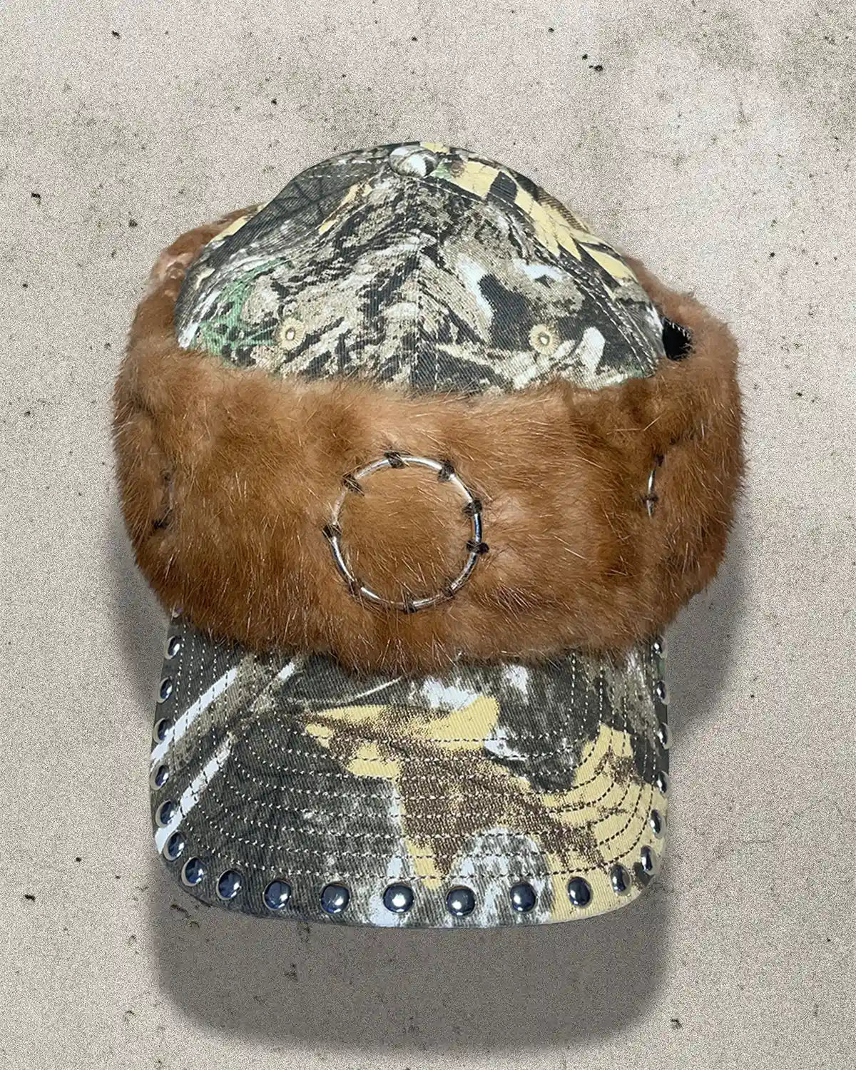 Camouflage visor with brown fur trim on a concrete surface