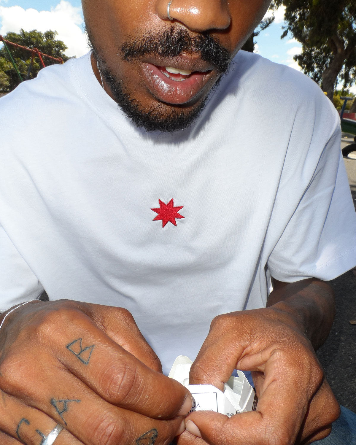 A tattooed man in a boxy white shirt, showcasing South African streetwear fashion by Bullyboy Apparel